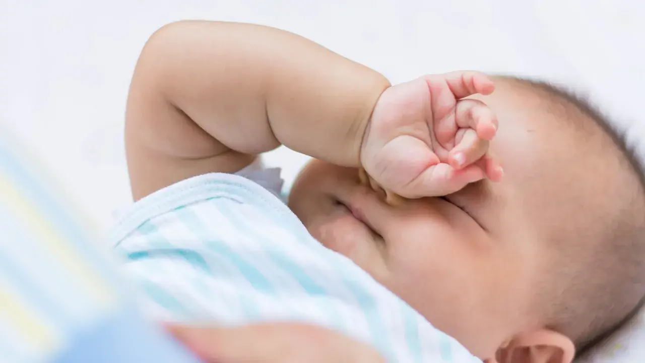 Baby im REM-Schlaf, die Hand vor den Augen, träumt süß.