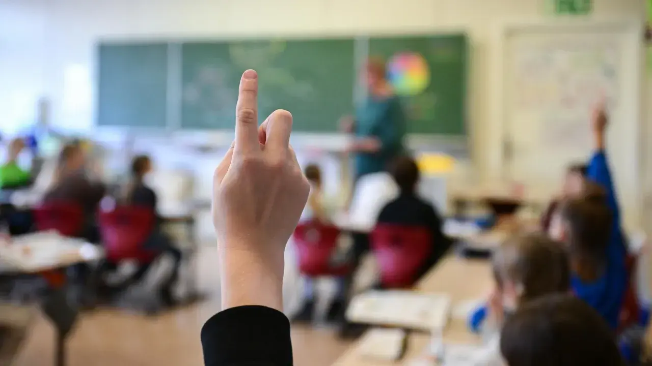 Ein Schüler hebt die Hand, um eine Frage zu stellen. Wie lange muss man in die Schule gehen? Die Antwort liegt im Unterricht.