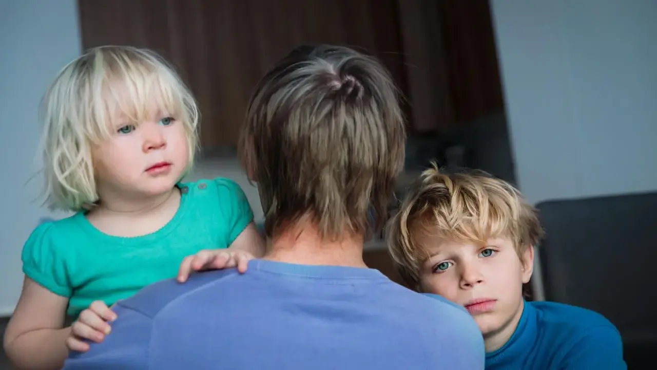 Zwei Kinder blicken besorgt über die Schulter einer Person. Die **Trennung wegen unterschiedlicher Erziehung** scheint sie zu belasten.