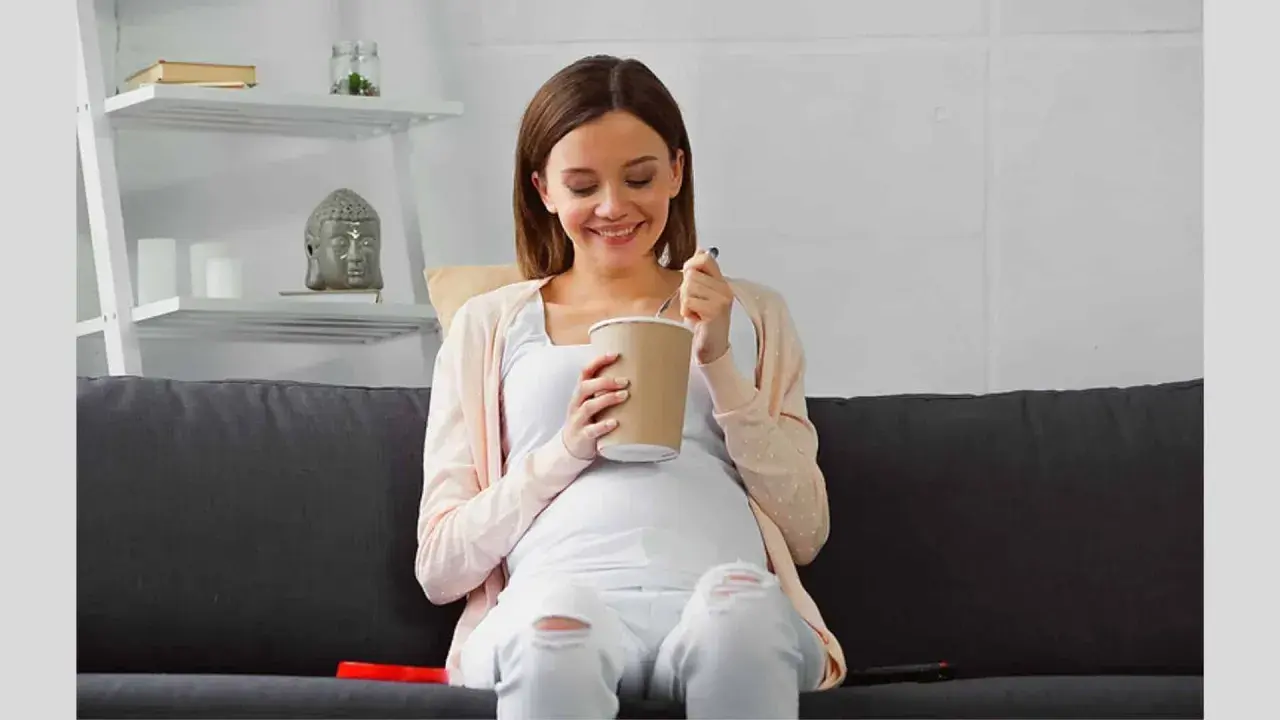 Lächelnde Schwangere isst Eis auf dem Sofa. Ein süßer Genuss während der Eis Schwangerschaft.