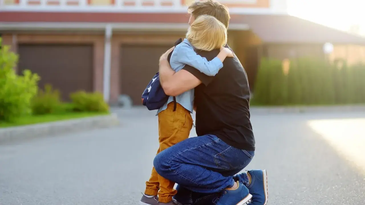 Vater umarmt seinen Sohn mit Rucksack. Ein guter Schulstart nach den Ferien beginnt mit einer liebevollen Umarmung.