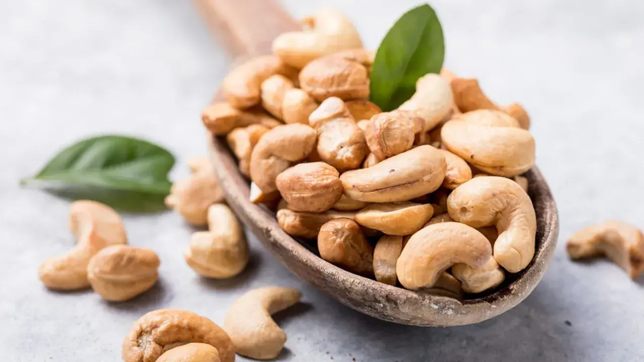 Holzkelle voller Cashewkerne, ideal für die Schwangerschaft. Zwei grüne Blätter liegen daneben.