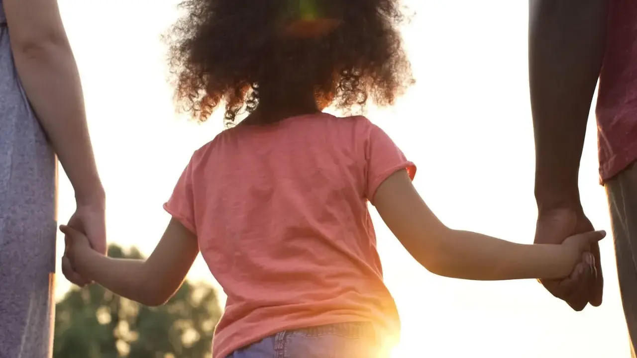 Kind hält Hände von Eltern. Die gesetzliche Regelung Kinderbetreuung Trennung soll das Wohl des Kindes sichern.