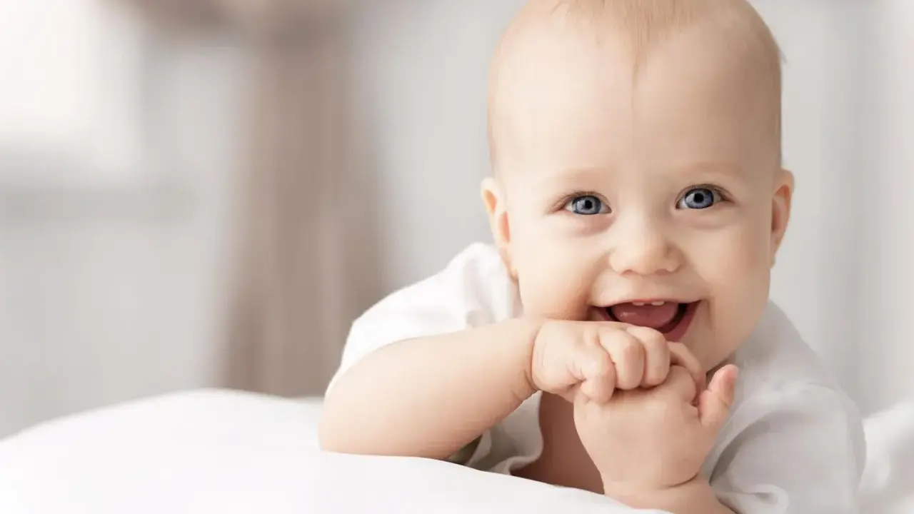 Ein lächelndes Baby mit blauen Augen, das auf einer weißen Decke liegt. Vielleicht ein zukünftiger Max oder Mika, einer der beliebten Jungennamen mit M.