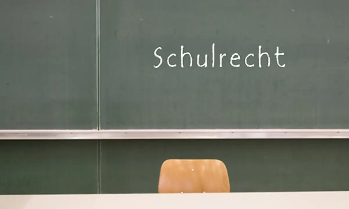 Grüne Tafel mit der Aufschrift "Schulrecht". Ein leerer Stuhl davor. Hier werden die Elternpflichten für Hausaufgaben und das Schulrecht thematisiert.