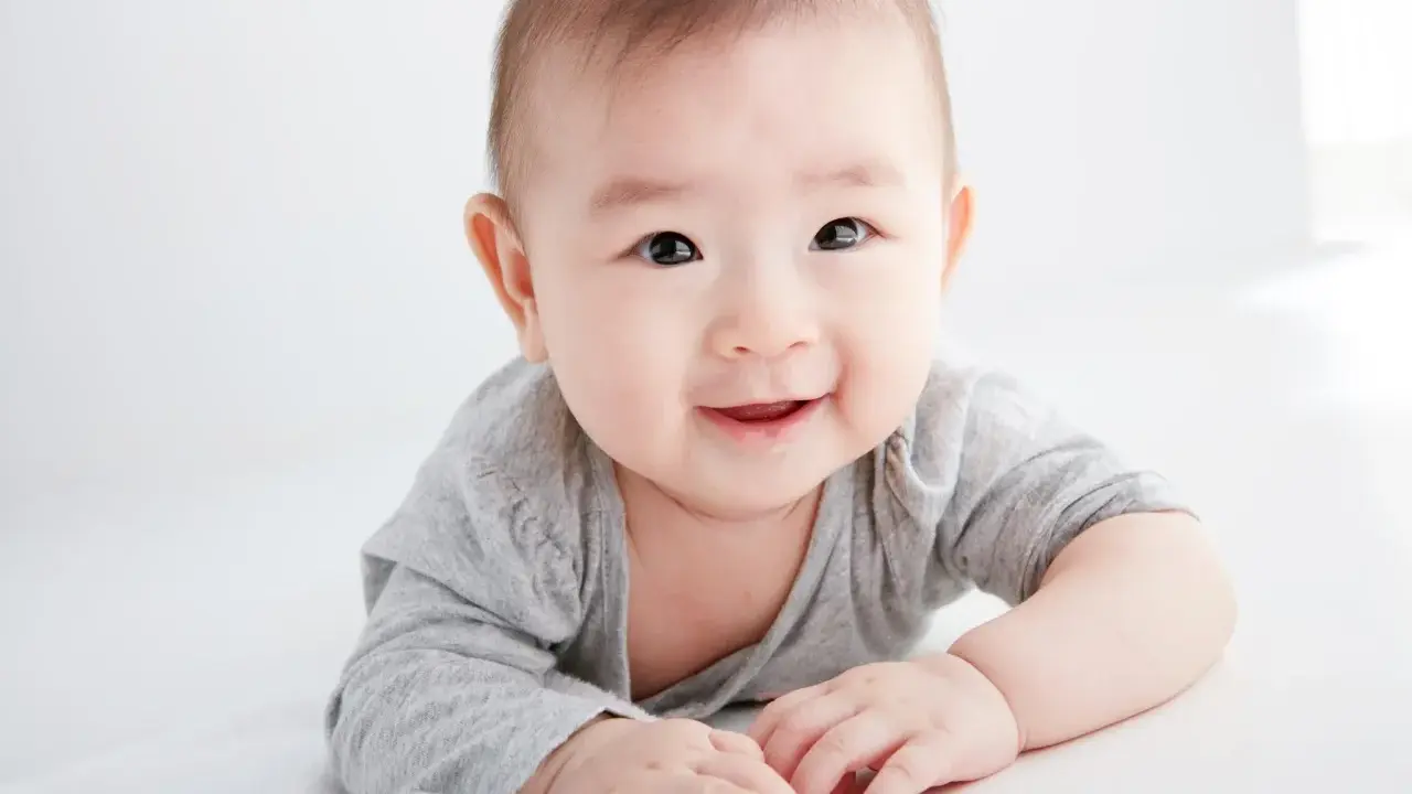 Lächelndes Baby in grauem Shirt auf weißem Hintergrund.