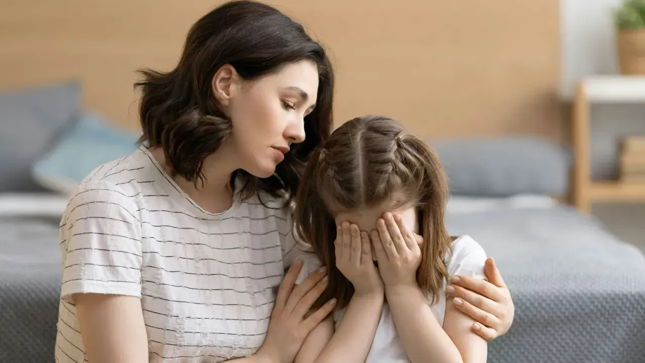 Eine Mutter tröstet ihr weinendes Kind, das sich die Augen zuhält. Möglicherweise kämpft das Kind mit Zwangsgedanken bei Kindern.