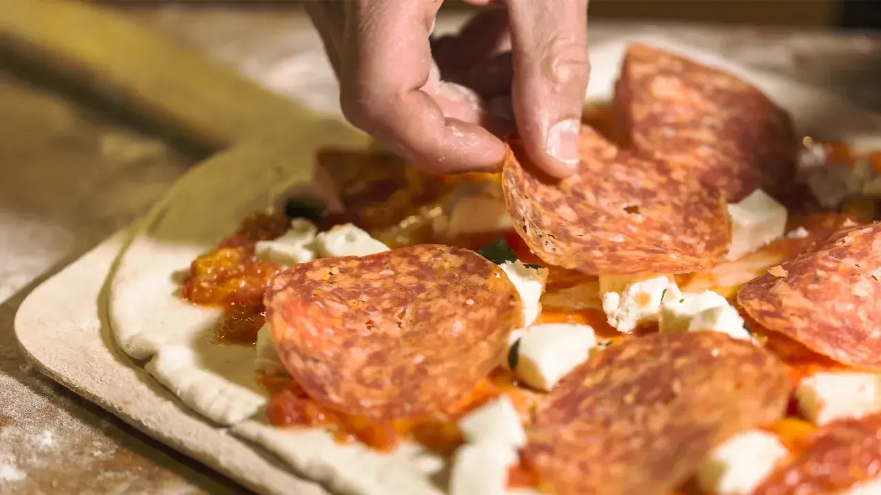 Hand belegt Pizza mit Salami. Frage: darf man in der schwangerschaft salami essen? Die Antwort ist ja, wenn sie gut durchgegart ist.