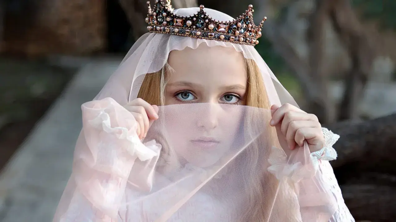 Ein Mädchen mit Krone und Schleier, wie eine Prinzessin aus Herr der Ringe Namen weiblich, blickt geheimnisvoll hervor.