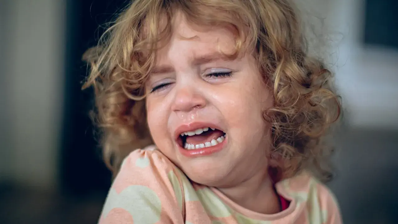Ein kleines Mädchen mit lockigen Haaren weint bitterlich. Tränen laufen über ihr Gesicht, die Augen sind geschlossen. Ein Ausdruck von starkem **Wut bei Kindern** ist deutlich zu sehen.