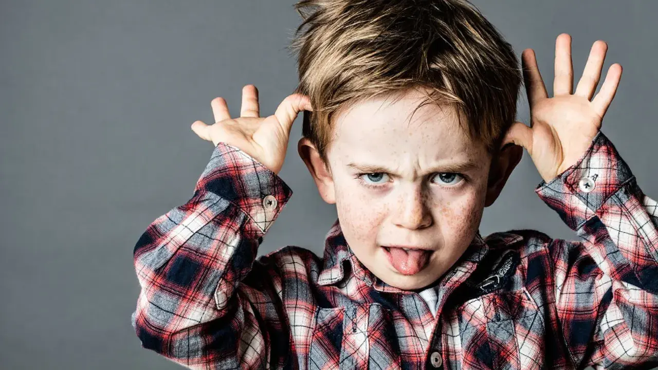 Ein frecher Junge mit Sommersprossen zieht Grimassen und steckt die Zunge heraus, ein Ausdruck dafür, wenn Kinder frech und respektlos sind.