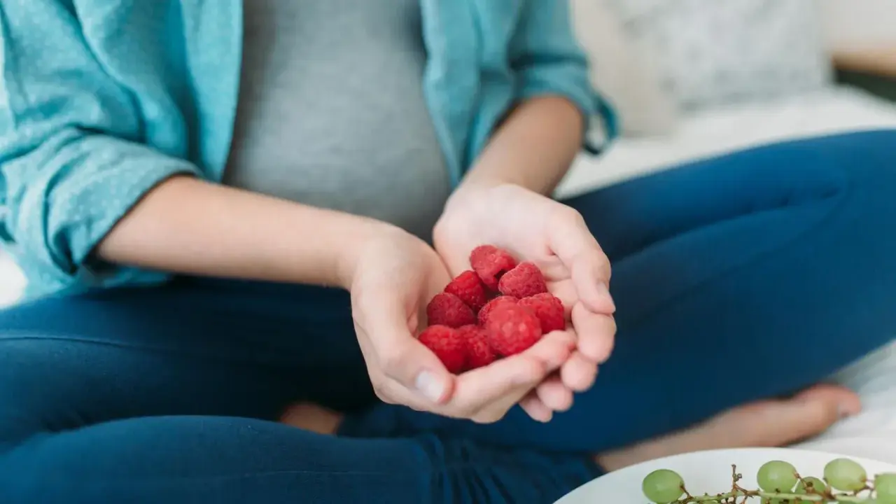 Schwangere Frau hält Himbeeren in den Händen. Die roten Früchte sind ein gesunder Snack während der Schwangerschaft.