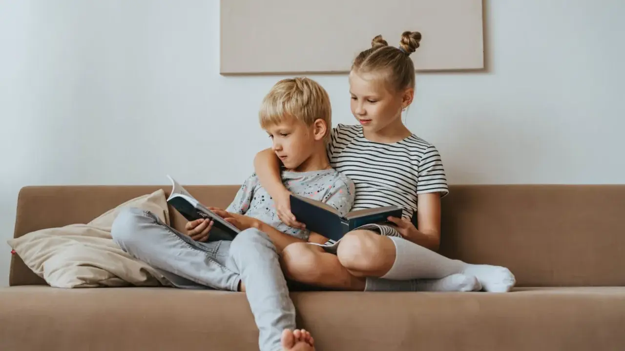 Geschwisterliebe: Ein Mädchen umarmt ihren Bruder, während sie gemeinsam auf dem Sofa lesen. Eine schöne Darstellung ihrer Beziehung.