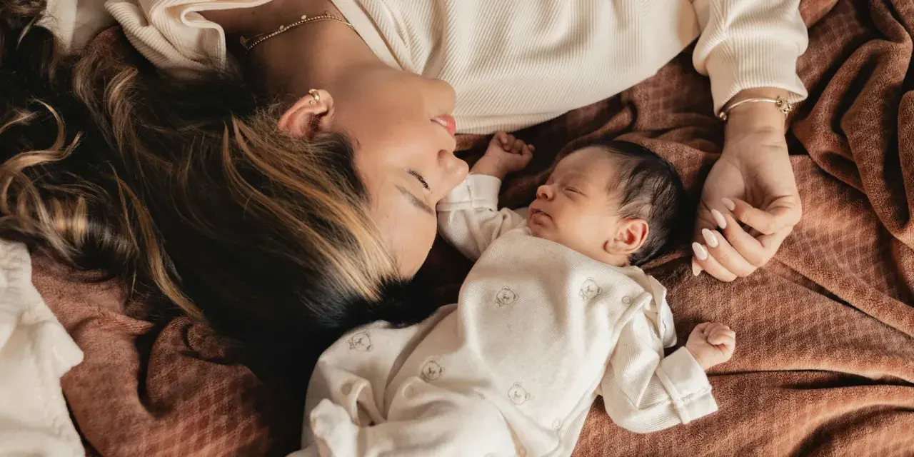 Mutter und Baby liegen eng beieinander. Die Mutter schaut liebevoll auf ihr schlafendes Kind. Ein Moment der Ruhe und Geborgenheit, der die **Baby-Begrenzung beim Schlafen** symbolisiert.