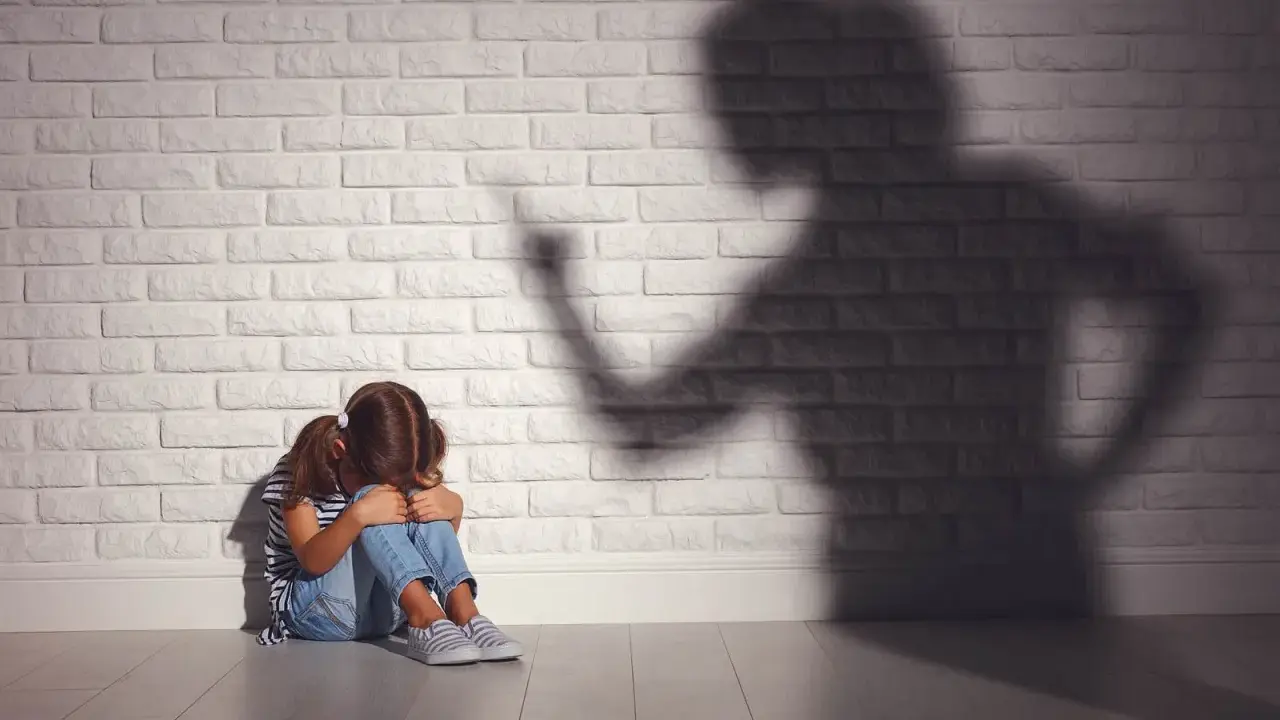 Ein Mädchen kauert weinend auf dem Boden, während ein bedrohlicher Schatten einer erwachsenen Person an der Wand steht. Psychologie: Mutter hasst Tochter?