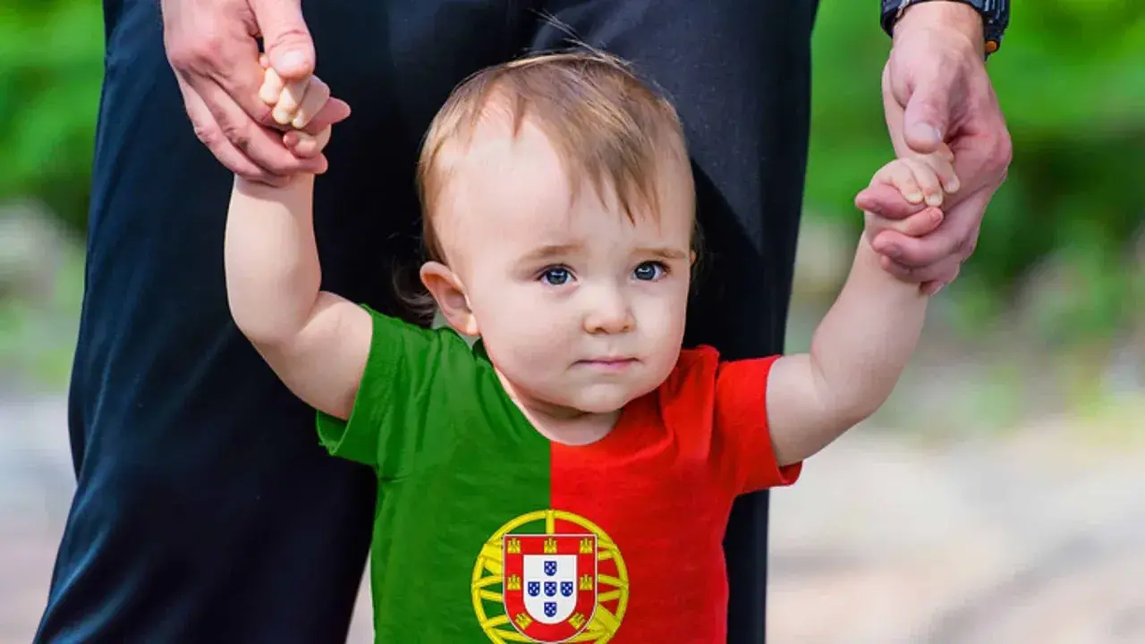 Ein süßes Baby mit portugiesischer Flagge auf dem T-Shirt, gehalten von einer Hand. Vielleicht ein zukünftiger João oder Miguel, inspiriert von portugiesischen Jungennamen.
