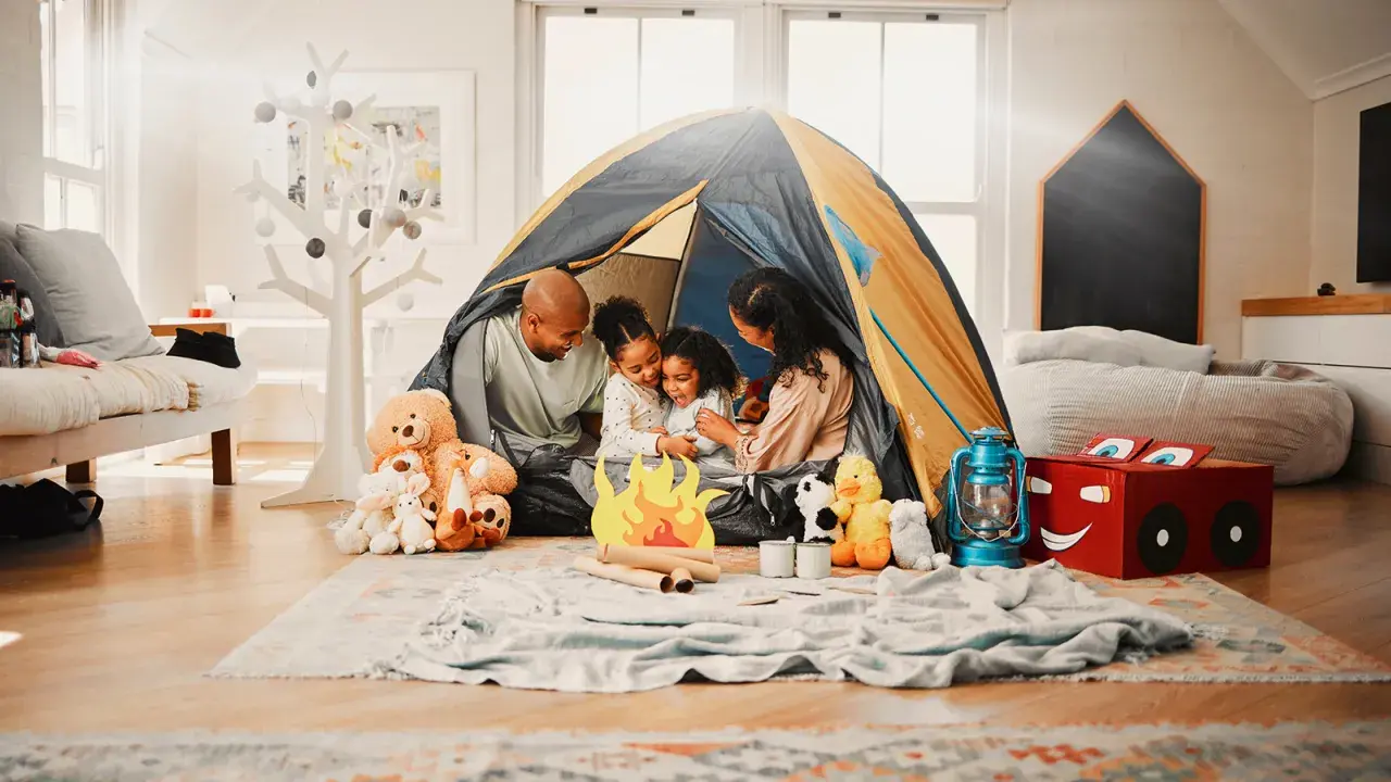 Familie verbringt **gemeinsame Zeit** beim Zelten im Wohnzimmer. Kinder kuscheln mit Teddybären, während Eltern lachen.