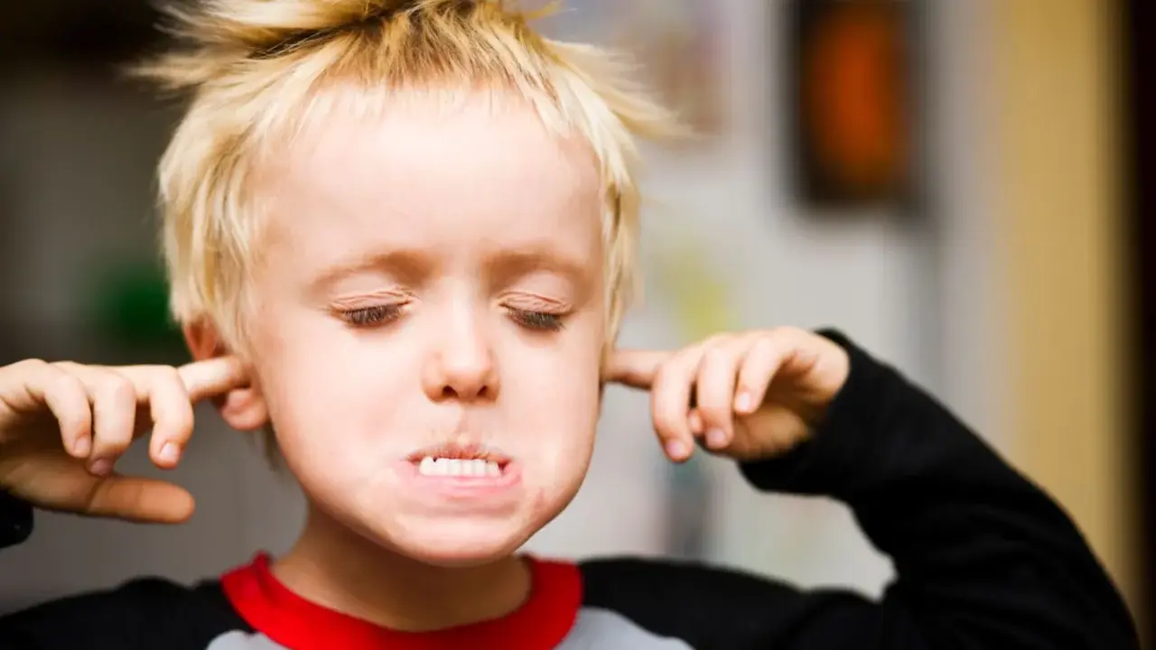 Ein Junge mit blonden Haaren stopft sich Finger in die Ohren, die Augen geschlossen, als ob er nichts hören will. Er verweigert alles.