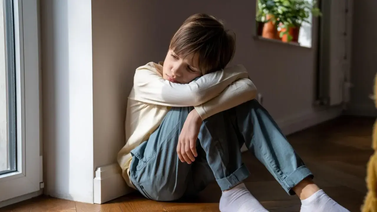 Ein trauriger Junge sitzt auf dem Boden. Wenn ein Kind nicht zur Schule geht, kann das ernste Konsequenzen haben.