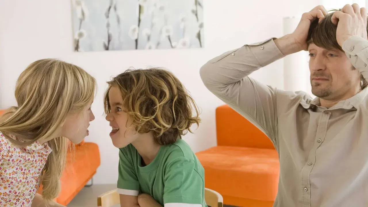 Zwei Kinder streiten sich heftig, während der Vater verzweifelt die Hände über dem Kopf zusammenschlägt. Ein Bild von Geschwisterhass und möglichen Erziehungsfehlern.