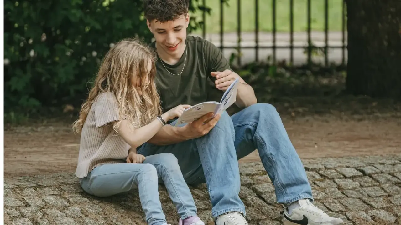 Ein junger Mann liest einem Mädchen im Park vor. Trotz der Trennung der Eltern finden die Kinder Trost und Nähe in gemeinsamen Momenten.