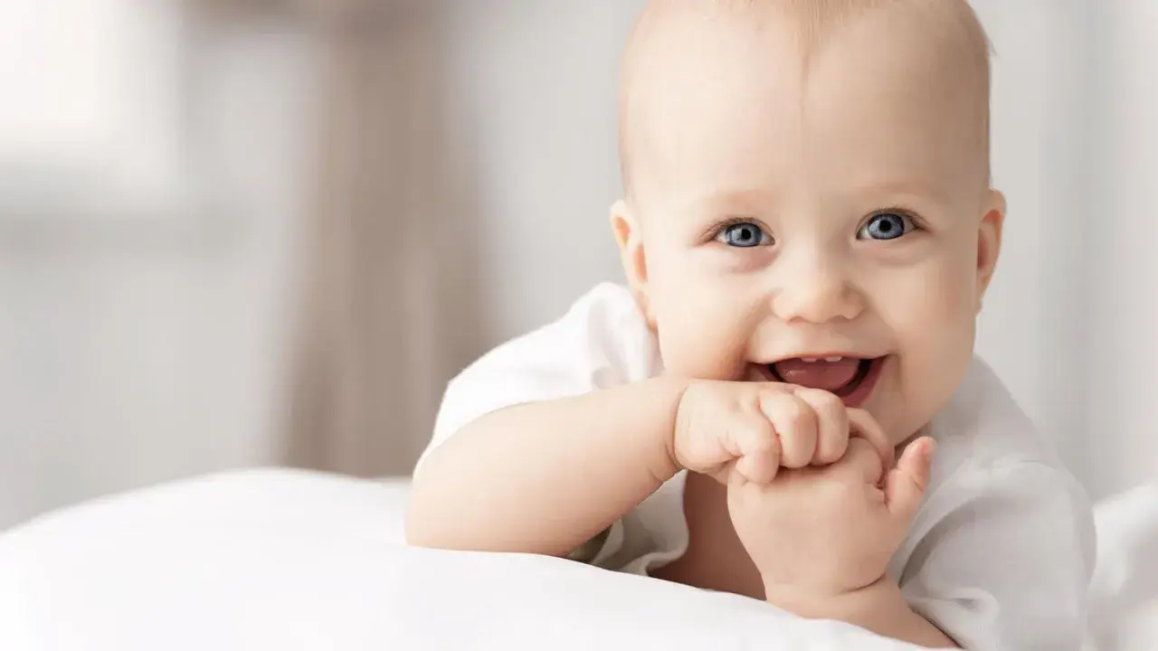 Ein lächelndes Baby mit blauen Augen, das auf einer weißen Decke liegt. Vielleicht ein zukünftiger Träger von langen Jungennamen wie Maximilian oder Alexander.