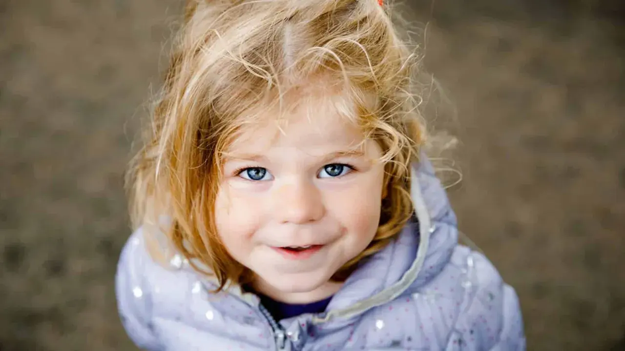 Ein blondes Mädchen mit blauen Augen lächelt. Ihr Haar ist zerzaust, wie bei vielen norddeutschen Frauennamen, die oft eine natürliche Schönheit widerspiegeln.