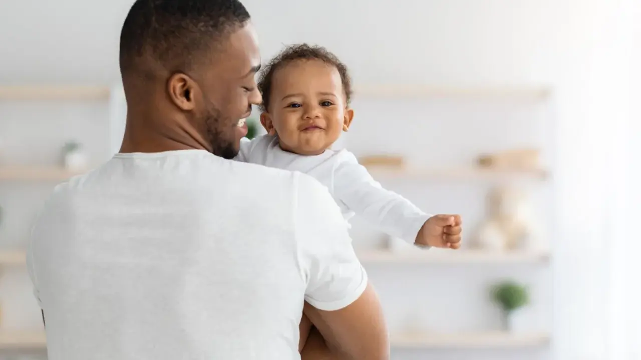 Ein Vater hält sein lächelndes Baby. Vielleicht sucht er nach christlichen Jungennamen für seinen kleinen Schatz.