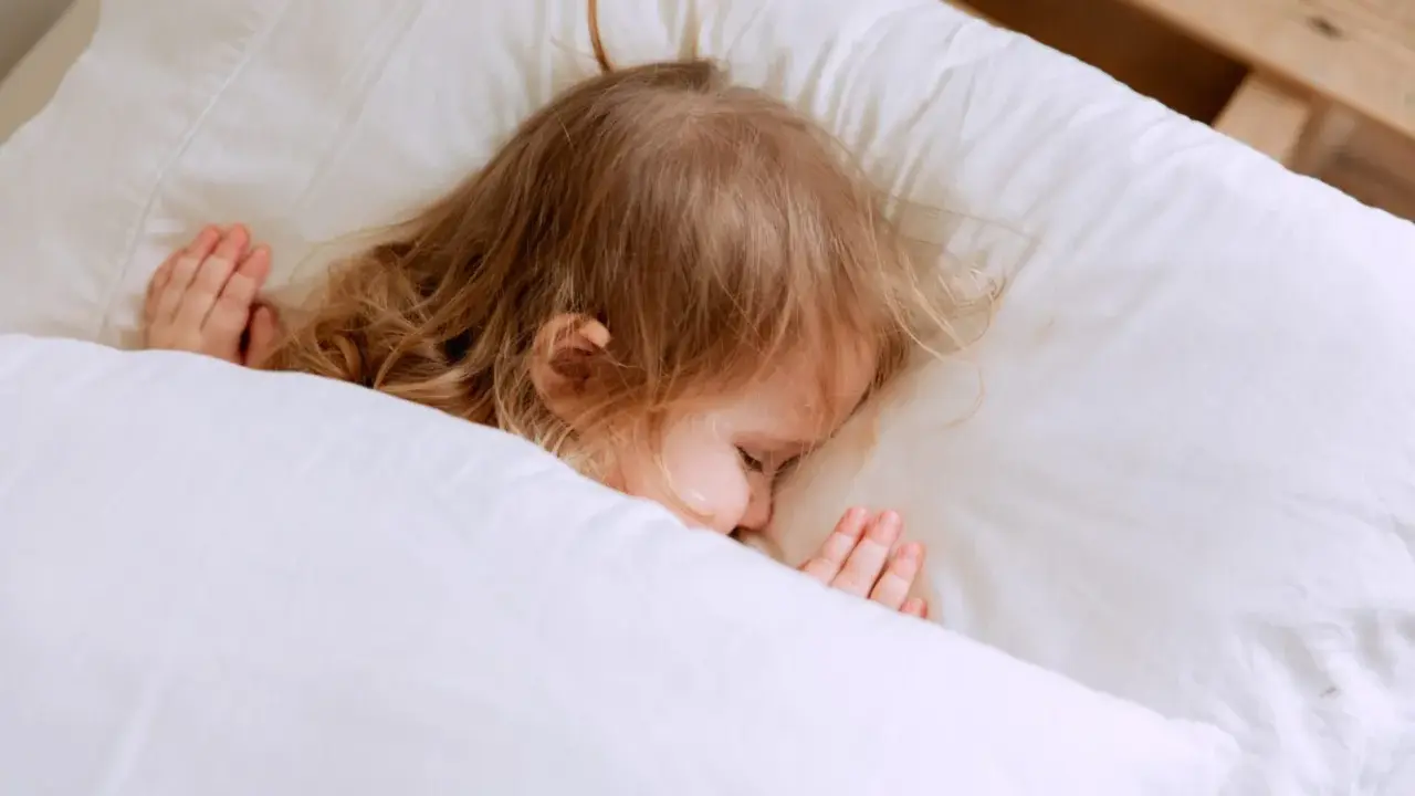 Kleines Kind schläft friedlich im Bett. Ab wann schlafen Kinder alleine ein? Diese süße Szene zeigt einen friedlichen Schlaf.
