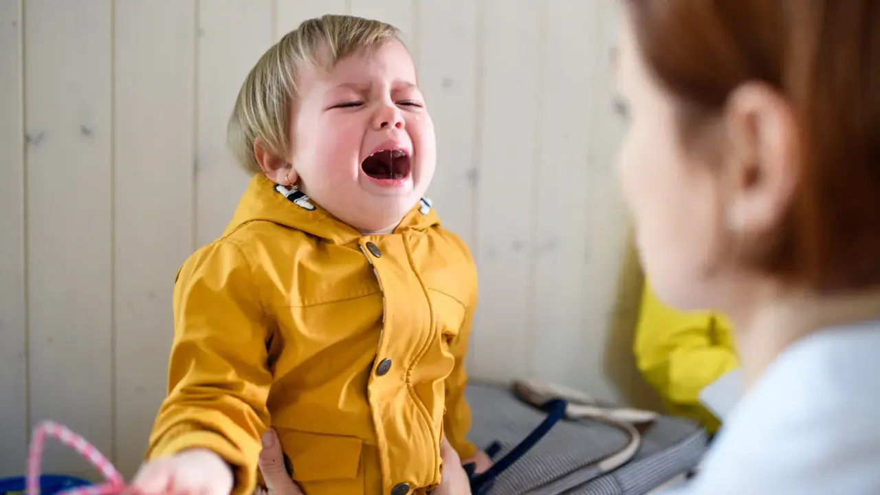 Ein weinendes Kind im Kindergarten, das nach Mama ruft. Die Erzieherin versucht, das kleine Mädchen zu trösten.