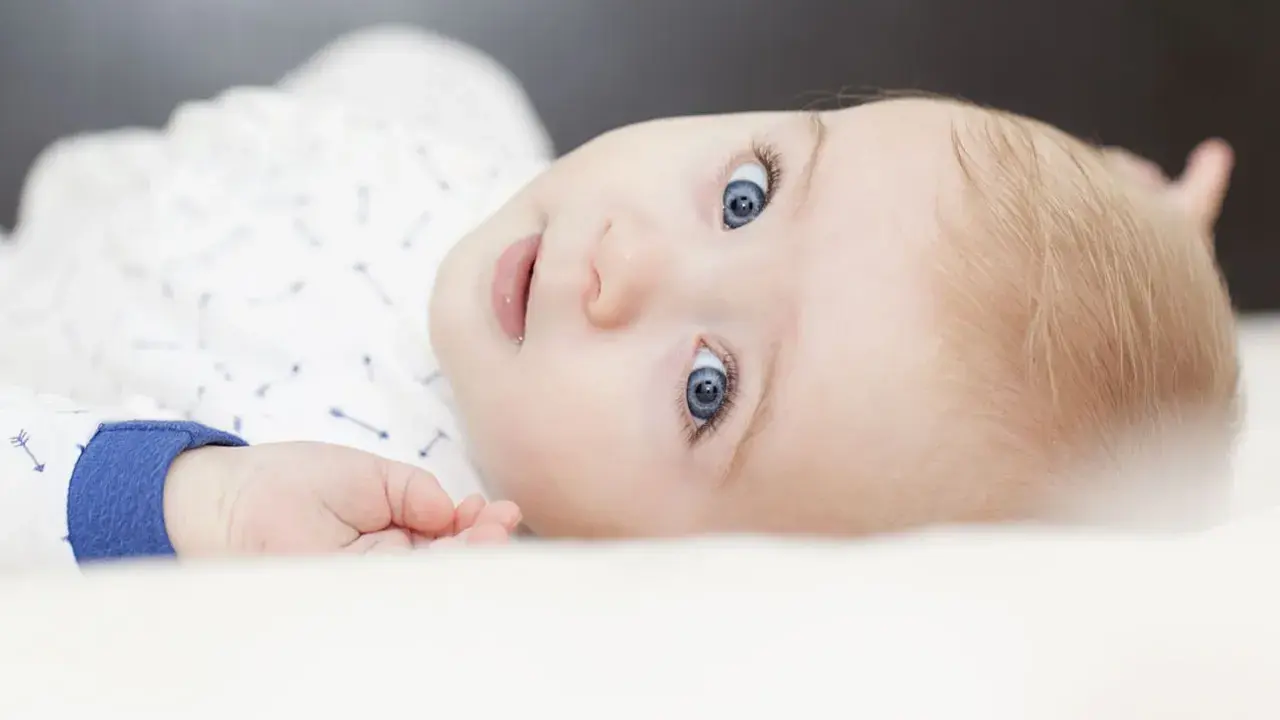 Ein Baby mit strahlend blauen Augen und blonden Haaren, das neugierig in die Kamera blickt. Ein süßer kleiner Kerl, der bestimmt mal einer der freche jungennamen tragen wird.