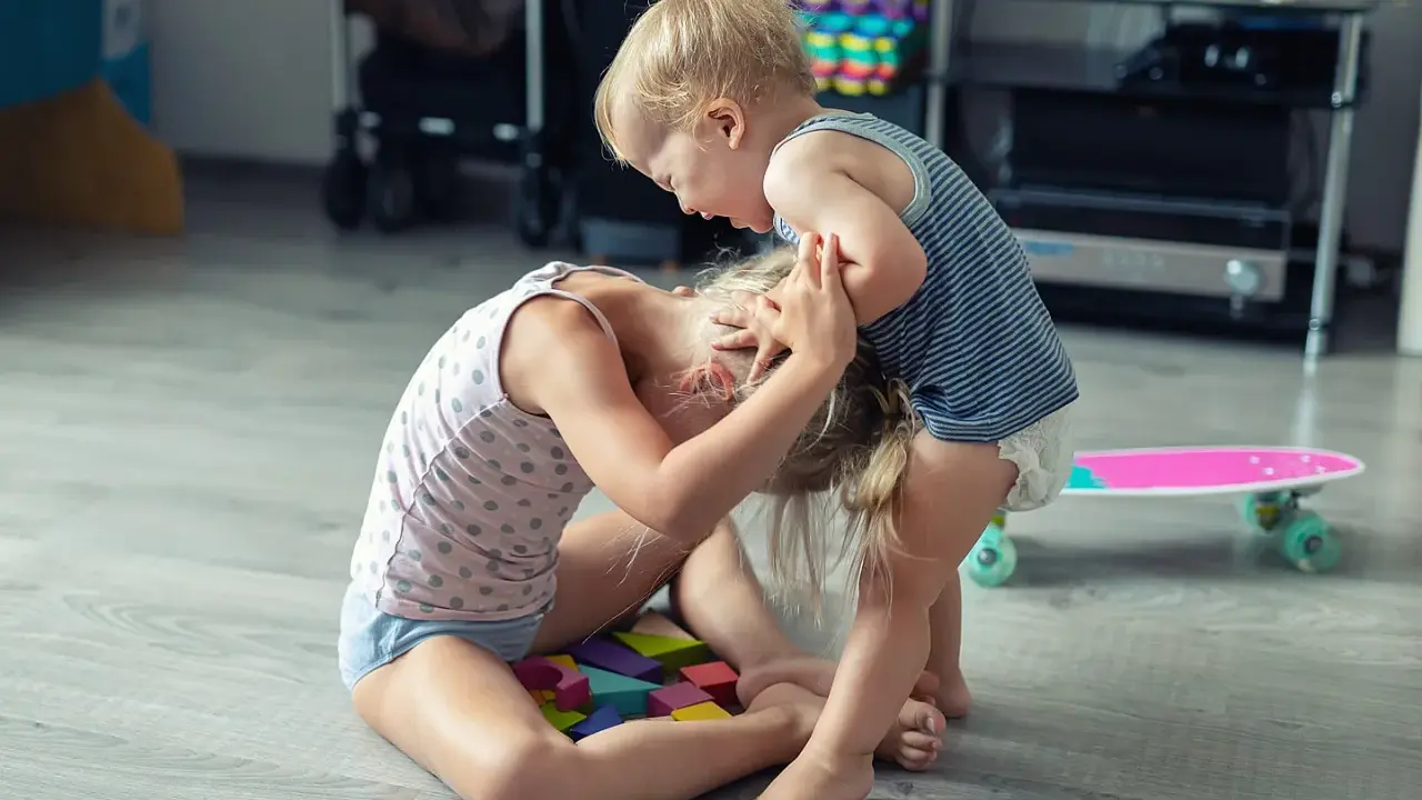 Ein aggressives Kind hält das Haar eines anderen Kindes, das auf bunten Holzklötzen sitzt.