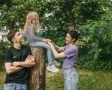 Ein junger Mann schaut zu seiner Mutter, die mit seiner kleinen Schwester auf einem Baumstumpf sitzt. Vielleicht denkt er, wenn der Sohn die falsche Freundin hat, ist die Familie trotzdem da.