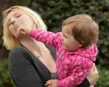 Ein kleines Kind haut sich selbst, die Mutter hält es.