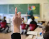 Ein Schüler hebt die Hand, um eine Frage zu stellen. Wie lange muss man in die Schule gehen? Die Antwort liegt im Unterricht.