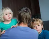 Zwei Kinder blicken besorgt über die Schulter einer Person. Die **Trennung wegen unterschiedlicher Erziehung** scheint sie zu belasten.