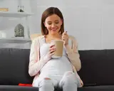 Lächelnde Schwangere isst Eis auf dem Sofa. Ein süßer Genuss während der Eis Schwangerschaft.