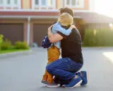 Vater umarmt seinen Sohn mit Rucksack. Ein guter Schulstart nach den Ferien beginnt mit einer liebevollen Umarmung.