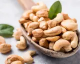 Holzkelle voller Cashewkerne, ideal für die Schwangerschaft. Zwei grüne Blätter liegen daneben.