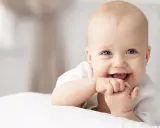 Ein lächelndes Baby mit blauen Augen, das auf einer weißen Decke liegt. Vielleicht ein zukünftiger Max oder Mika, einer der beliebten Jungennamen mit M.