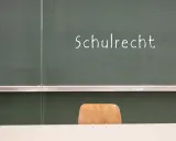 Grüne Tafel mit der Aufschrift "Schulrecht". Ein leerer Stuhl davor. Hier werden die Elternpflichten für Hausaufgaben und das Schulrecht thematisiert.