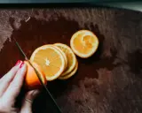 Eine Hand mit roten Nägeln schneidet Orangen auf einem Holzbrett. Orangen in der Schwangerschaft sind eine gesunde Wahl.