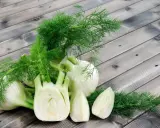 Frischer Fenchel, bekannt für seine verdauungsfördernden Eigenschaften, ist eine beliebte Wahl während der Schwangerschaft. Hier liegen ganze und angeschnittene Knollen auf Holzbrettern.