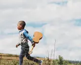 Ein kleiner Junge, vielleicht 18 Monate, rennt mit einer Ukulele durch die Natur. Ein sehr anstrengender, aber glücklicher Moment.