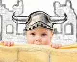 Kleines Wikinger-Baby mit Helm vor einer Burgkulisse. Vielleicht ein zukünftiger Held mit einem Namen wie Astrid oder Freya?