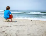 Ein Junge sitzt allein am Strand auf einem Fußball. Er blickt aufs Meer. Meine Tochter 16 hat keine Freunde, sie fühlt sich oft so einsam.