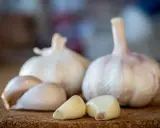 Frische Knoblauchzehen und ganze Knoblauchknollen liegen auf einer korkartigen Oberfläche. Knoblauch in der Schwangerschaft kann eine gesunde Ergänzung sein.