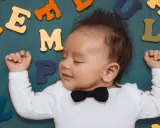 Schlafender Junge mit Fliege, umgeben von bunten Buchstaben. Vielleicht ein zukünftiger Paul oder Peter?