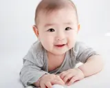 Lächelndes Baby in grauem Shirt auf weißem Hintergrund.