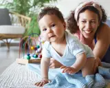 Ein Baby krabbelt neugierig, seine Mutter lächelt. Ein starker Wille zeigt sich schon früh, die Bedeutung des Namens wird gelebt.